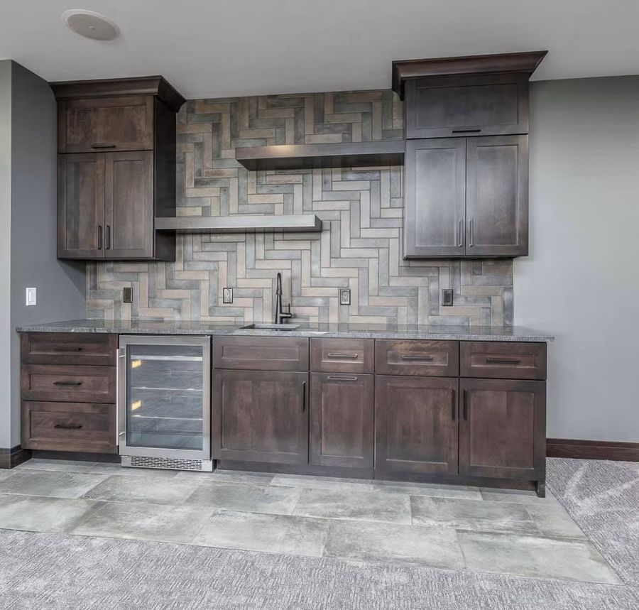 Finished basement wet bar with herringbone tile backsplash and beverage cooler