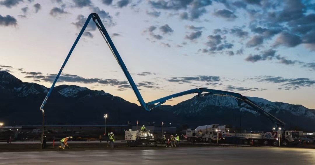 Concrete pump boom placing a large slab pour at dusk